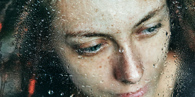 Uma mulher atrás de um vidro com inúmeras gotas de água